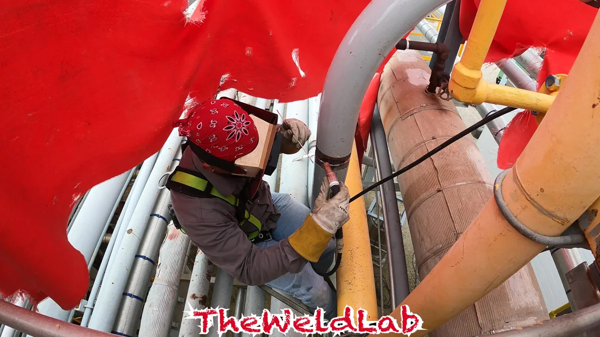 Welder working on industrial piping from an elevated platform